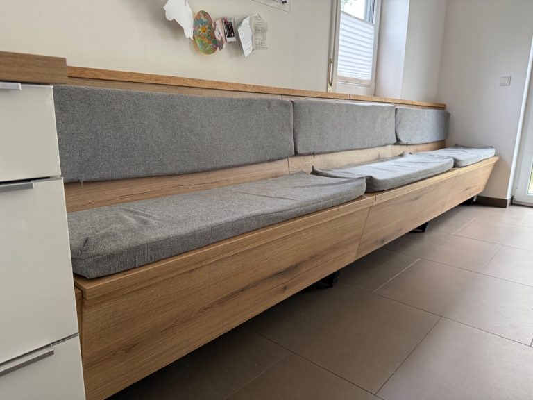 Sitzbank Lange, moderne Sitzbank mit grauen Kissen in einem hellen Raum.