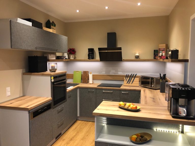 Moderne Küche mit Holzoberflächen, Herd, Kühlschrank und beleuchtetem Arbeitsbereich.