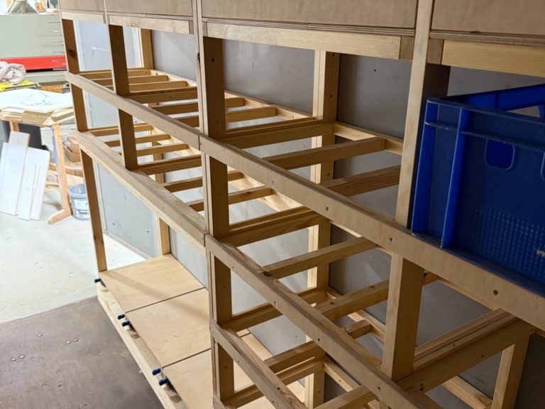 Ausbau eines PKW- Anhängers zur mobilen Werkstatt Holzregal mit offenen Fächern, teilweise leer, in einem Anhänger.
