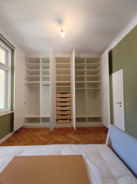 Ein leerer Raum mit einem weißen Kleiderschrank und Holzboden, fliederfarbener Wand.