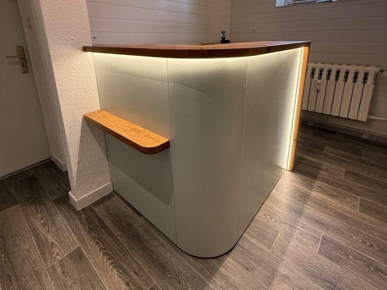 Moderne Empfangstheke mit Holz- und Lichtakzenten in einem hellen Raum.