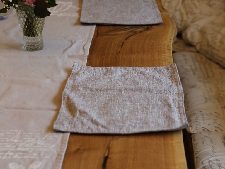 Esstisch aus Eiche - gefertigt in unserer Tischlerei in Wurzen Platzdeckchen in neutralen Farben auf einem Holztisch mit einer Blumenvase im Hintergrund.