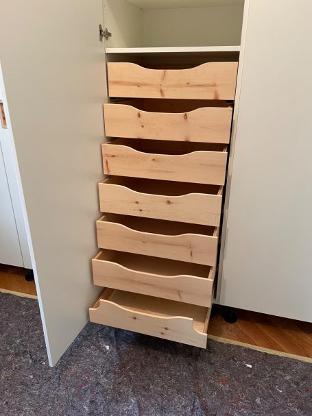Schrank mit sieben Holzschubladen, offen, in einem hellen Raum.