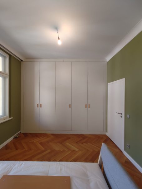 Helles Zimmer mit schlichten Möbeln, grüner Wand und weißem Schrank.