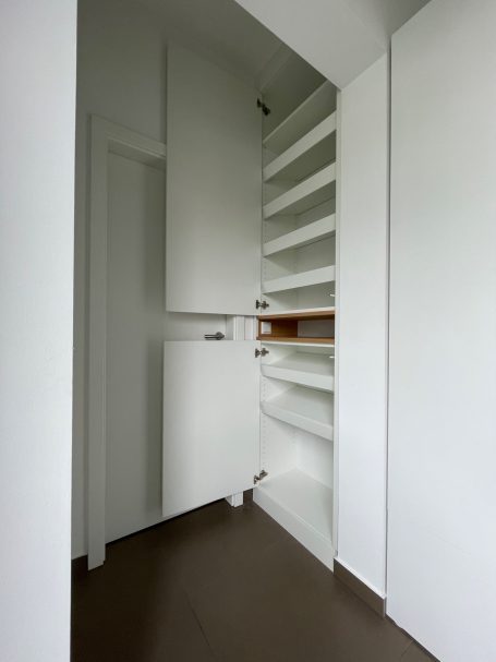 Weißer Wandschrank mit offenen Regalen und Tür.