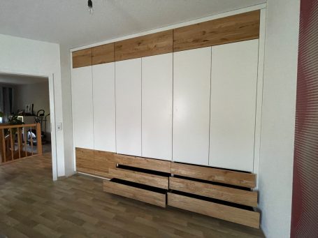 Wandregal in heller Holzoptik mit weißen Türen und darunterliegenden Schubladen.